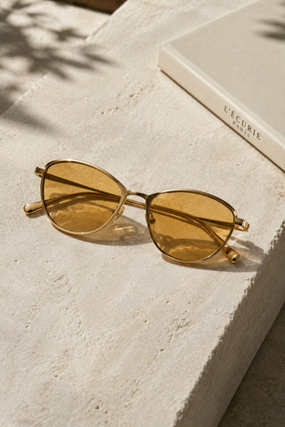 L'Écurie Paris gold cat-eye sunglasses with amber lenses on travertine